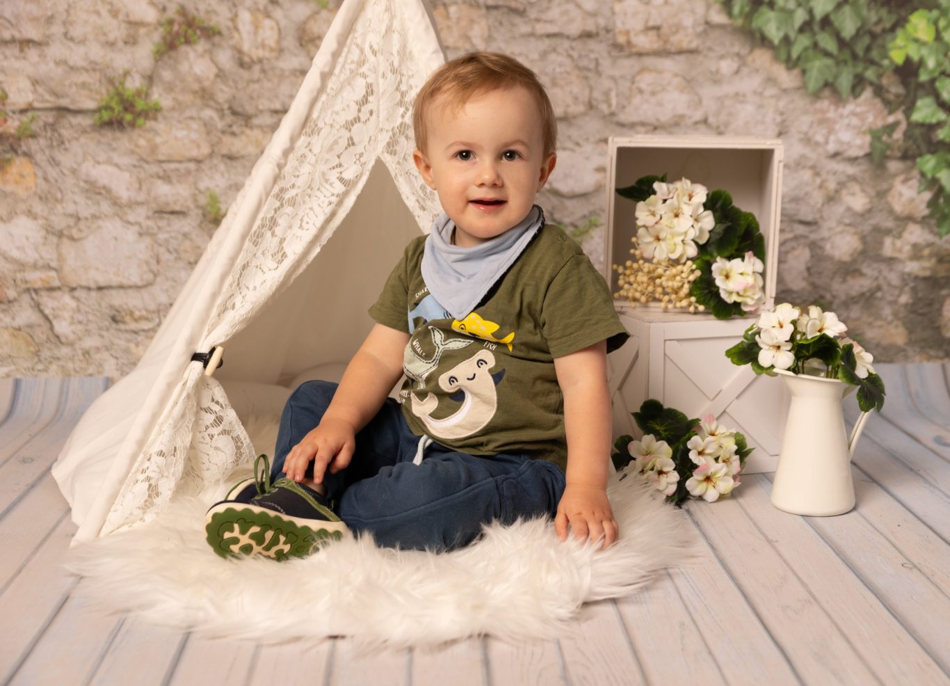 Kleiner Junge sitzt fröhlich in einem Zelt, umgeben von Blumen und Deko.