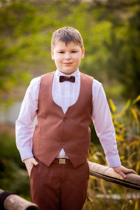 Ein Junge in festlichem Anzug mit Fliege steht lächelnd im Freien.