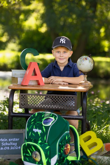 Ein Junge sitzt an einem Tisch mit Buchstaben, einem Globus und einem Rucksack im Freien.