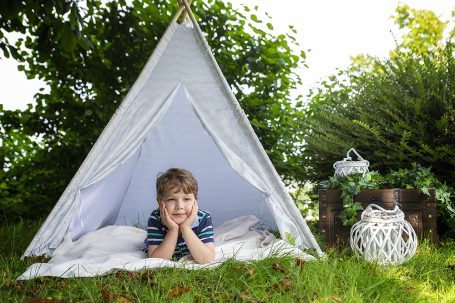 Ein Junge liegt entspannt in einem Zelt aus Stoff auf dem Gras, umgeben von Pflanzen.