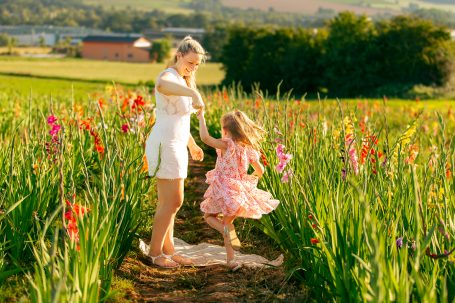Eine Frau und ein Mädchen tanzen fröhlich in einem blühenden Blumenfeld.