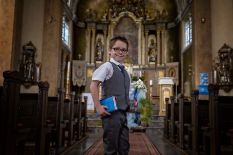 Ein kleiner Junge in einer Kirche hält ein Buch und schaut lächelnd in die Kamera.