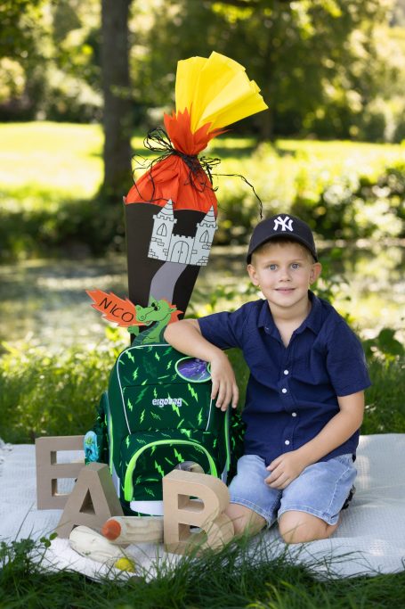 Ein Junge sitzt neben einem Schulranzen mit bunten Dekorationen und Buchstaben.