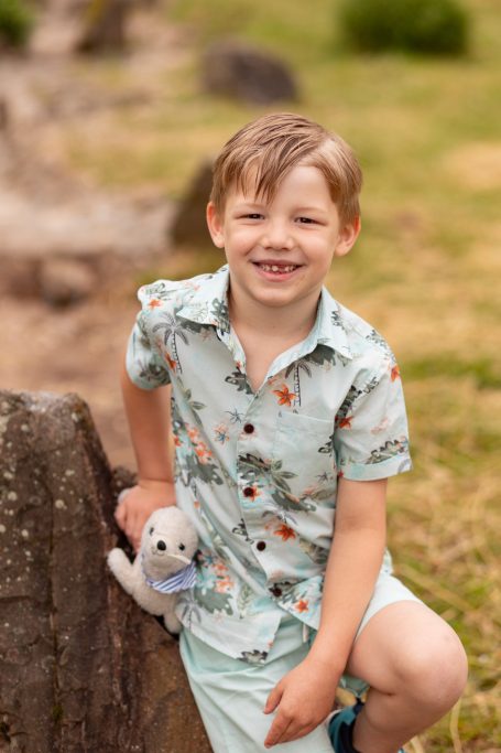 Ein lächelnder Junge in einem hellen Hemd hält ein Spielzeugseelchen und sitzt im Freien.