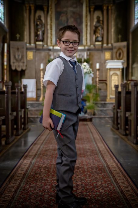 Ein Junge in Anzug steht in einer Kirche mit Buch in der Hand.