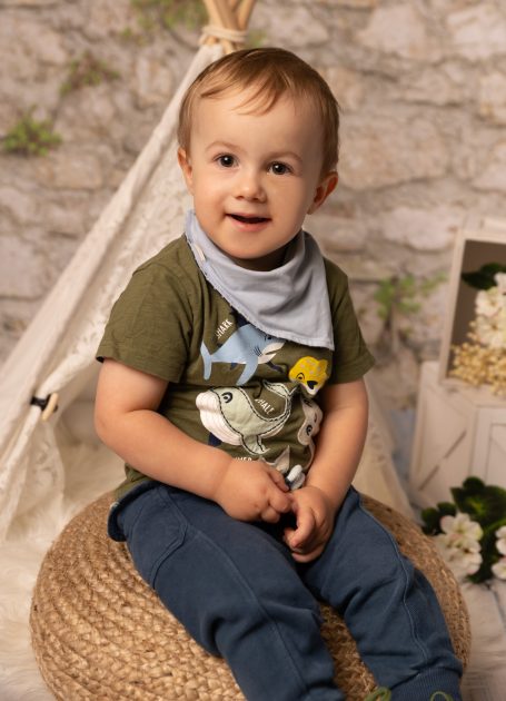 Ein lächelnder Kleinkind sitzt auf einem Sessel und trägt ein T-Shirt mit Tiermotiven.