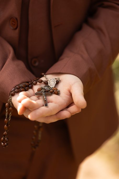 Händed mit einer Kette und einem Kreuz, elegant gekleidet in Braun.