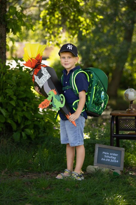 Ein Junge mit einem Rucksack und einer bunten Wasserpistole in einem Garten.