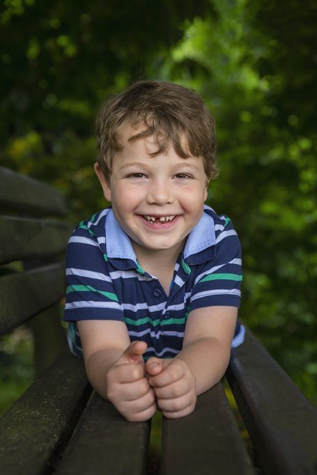 Lächelnder Junge in gestreiftem T-Shirt sitzt auf einer Bank im Freien.