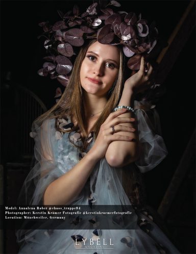 Junge Frau mit floralem Haarschmuck, sanft lächelnd, in einem transparenten Kleid.