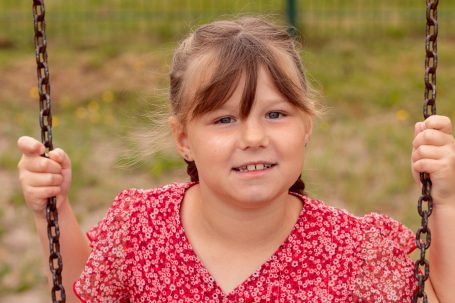 Mädchen auf einer Schaukel, lächelt in einem roten, gemusterten Kleid.