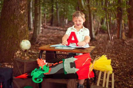 Ein lächelnder Junge sitzt an einem Tisch im Wald und hält den Buchstaben A.