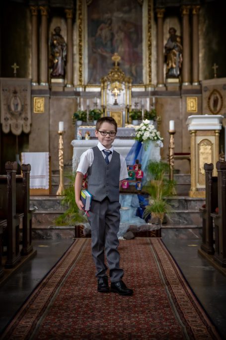 Ein Junge in Anzug steht in einer Kirche mit Blumenarrangements im Hintergrund.